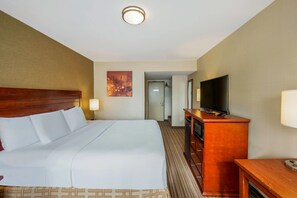 A hotel room with a large bed, a television on a wooden cabinet, and a door leading to another room.