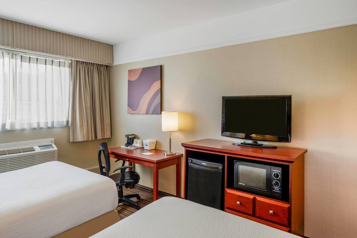 A hotel room with two beds, a desk with a lamp, a television, a mini-fridge, and a microwave.