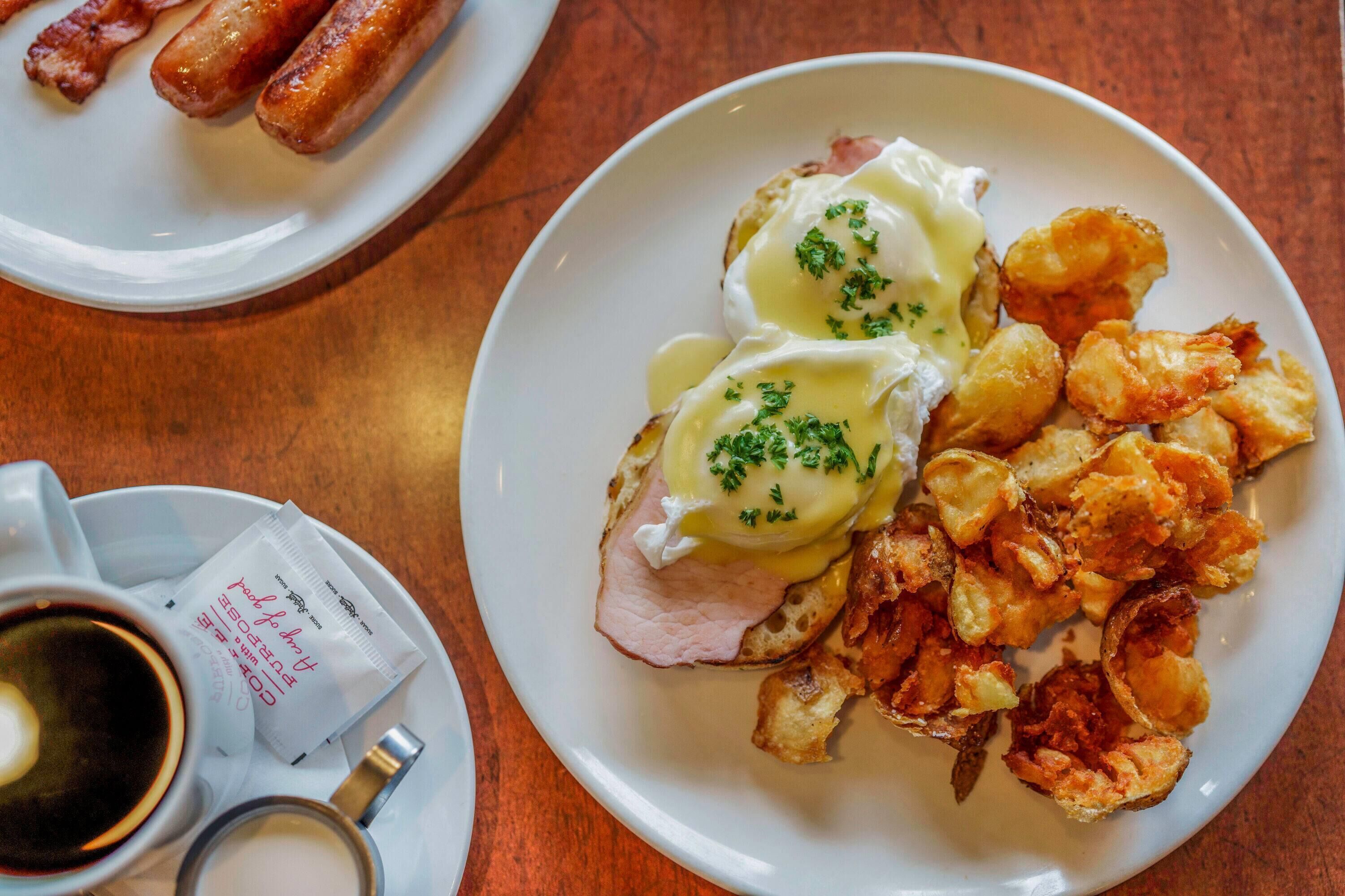 A breakfast plate with eggs benedict, hash browns, and sausages.