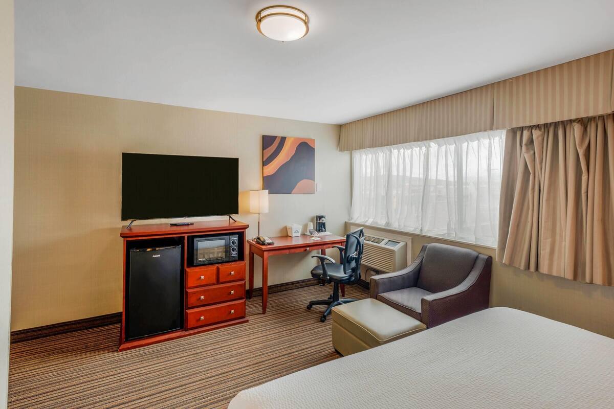 A hotel room with a bed, a desk with a computer, a television, a refrigerator, and a chair.
