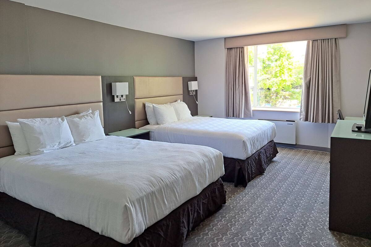 A hotel room with two beds, a desk, and a window with curtains.