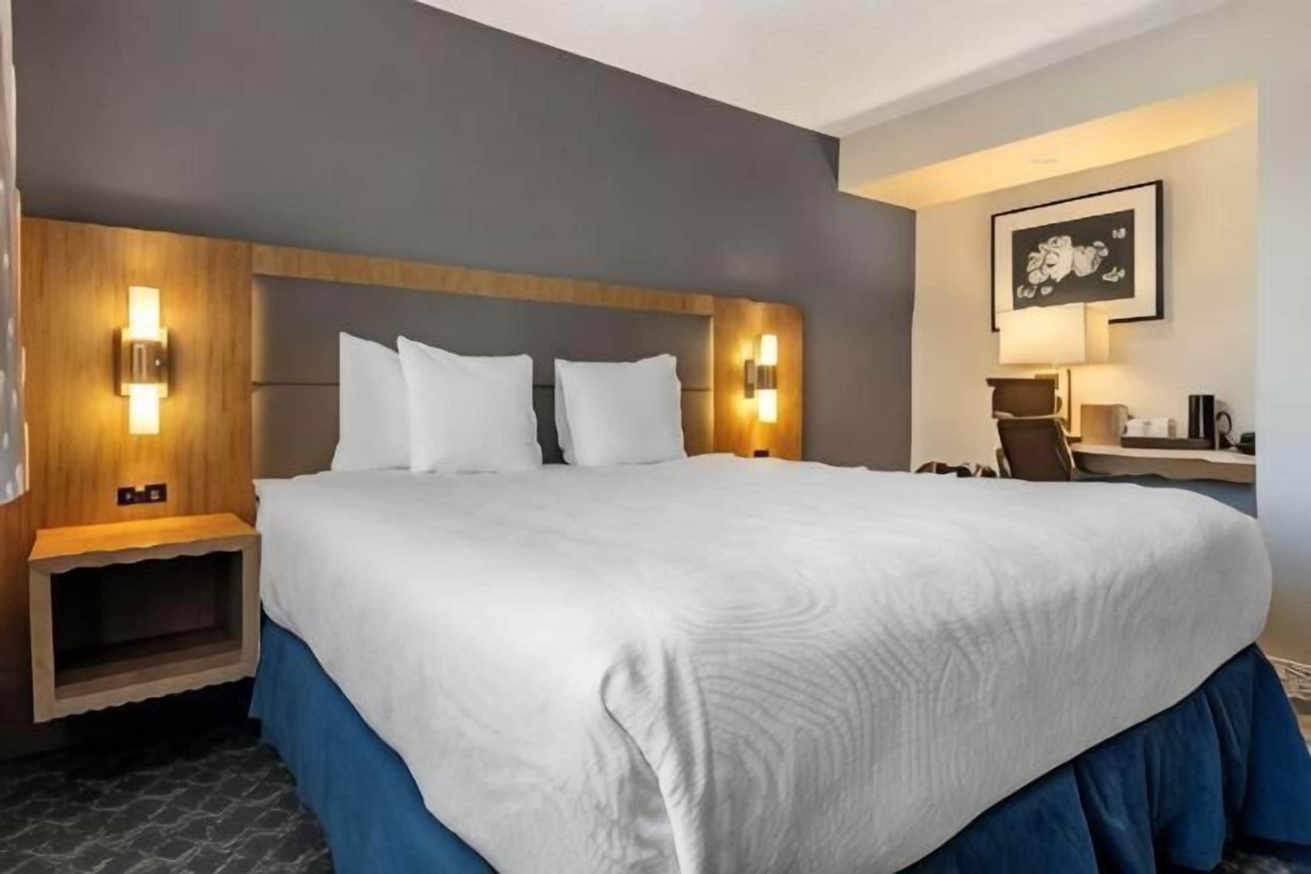 Une chambre d’hôtel avec un grand lit, des lampes de chevet, un bureau avec une chaise et un tableau encadré au mur.