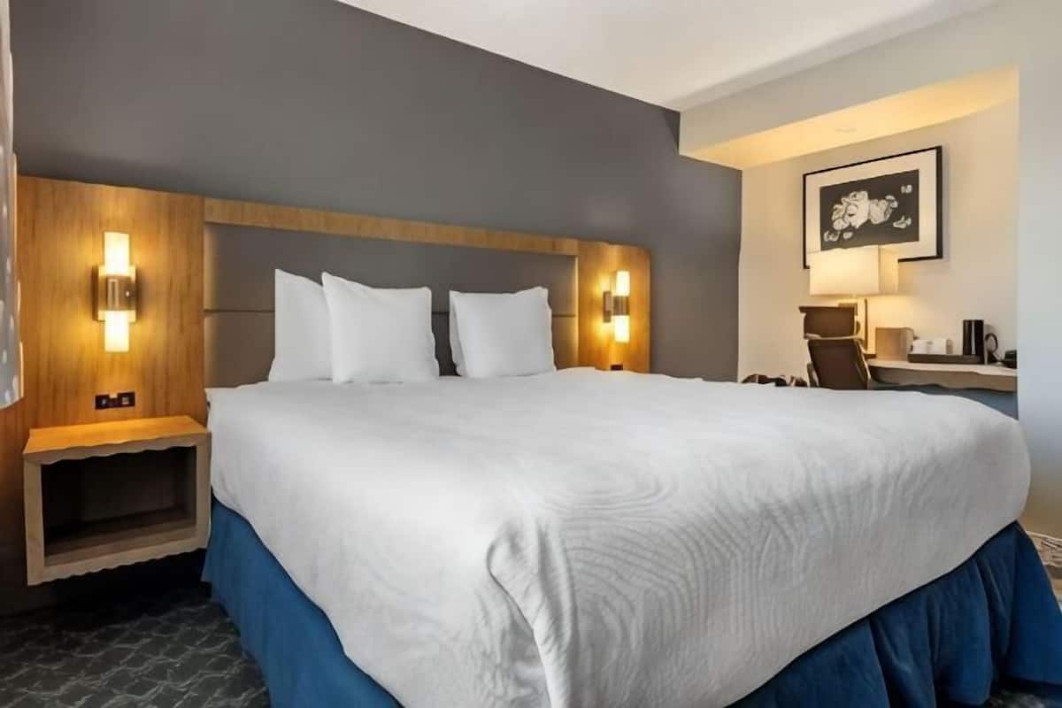 Une chambre d’hôtel avec un grand lit, des lampes de chevet, un bureau avec une chaise et un tableau encadré au mur.