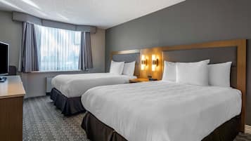 A hotel room with two beds, a desk, a TV, and a window with curtains.