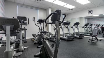 A gym with various cardio machines, including treadmills and elliptical trainers, arranged in rows.
