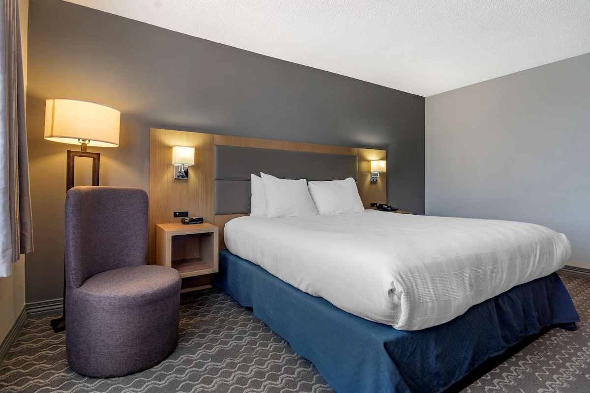 A hotel room with a large bed, a chair, a nightstand, and two wall-mounted lamps.