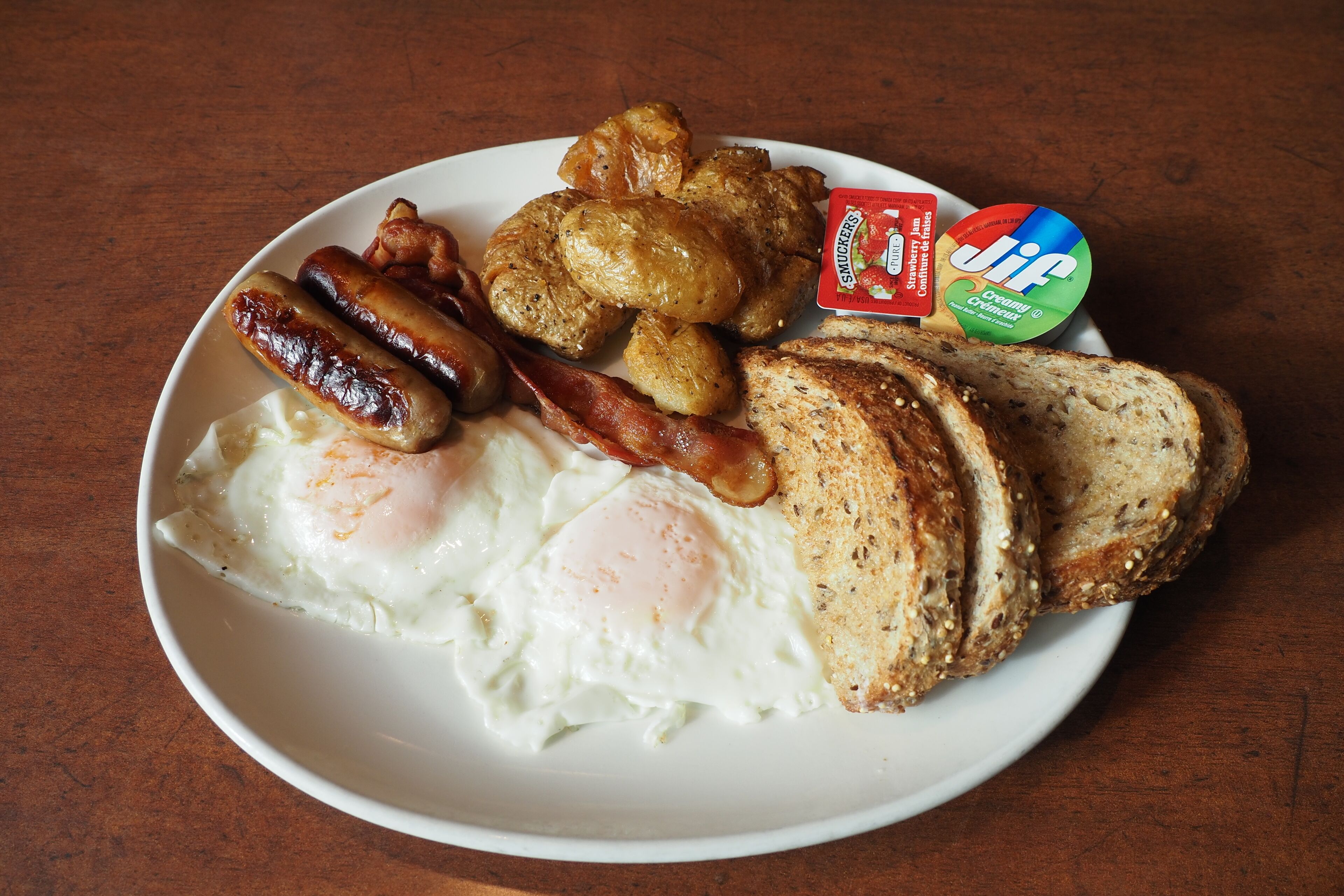 A plate with eggs, sausages, bacon, toast, and a packet of Jif cream cheese.