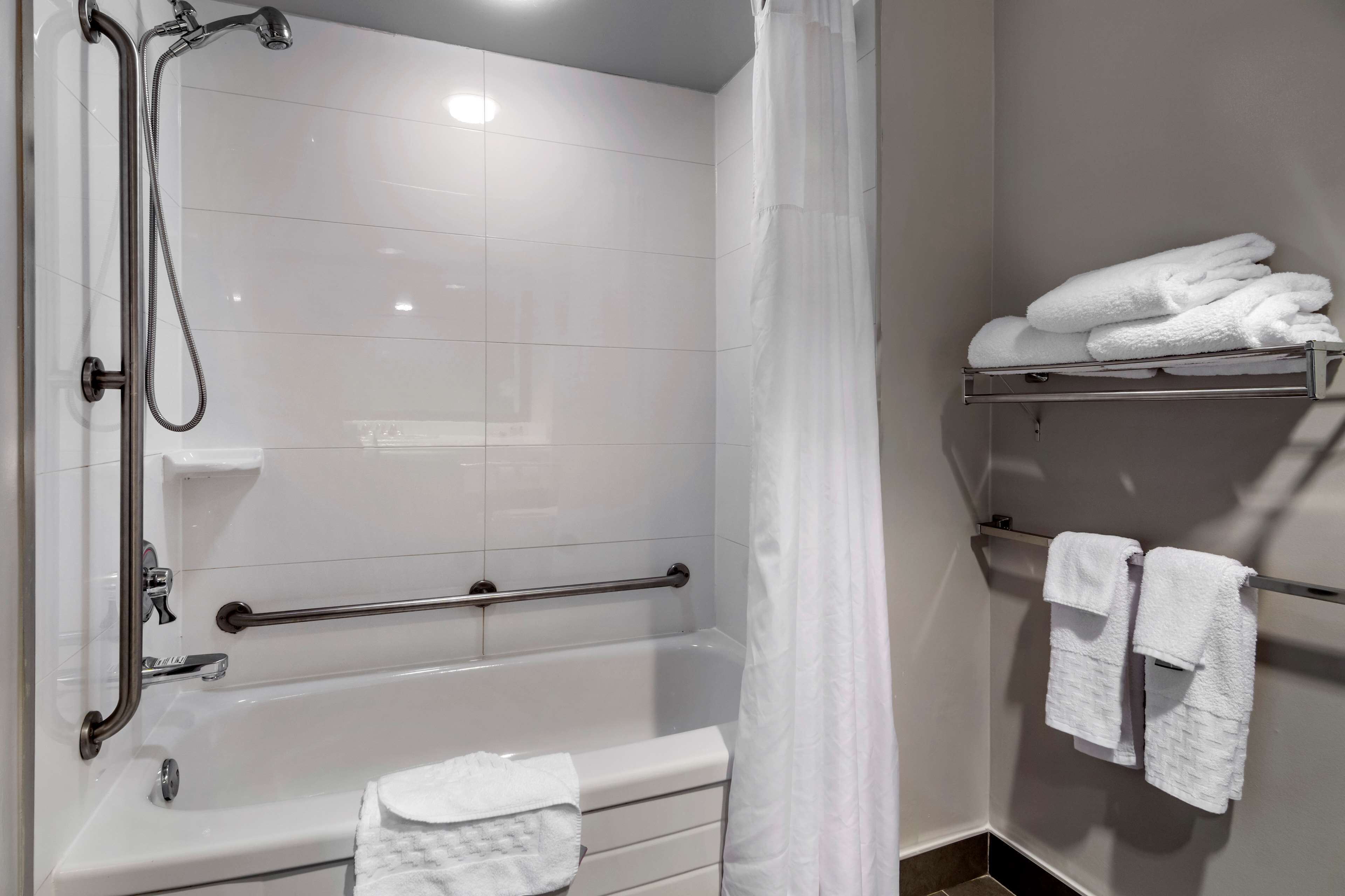 A bathroom with a bathtub, a shower with a handheld showerhead, a grab bar, and a towel rack with towels.