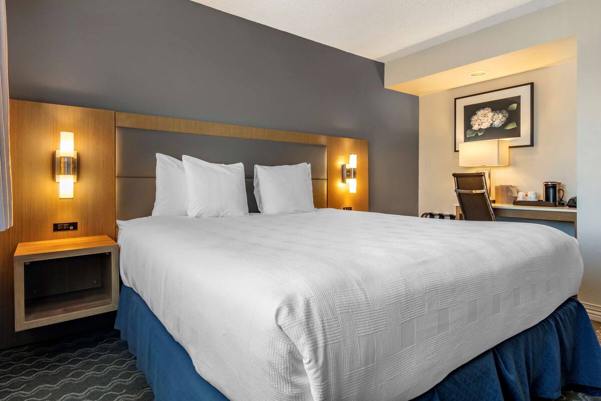 A hotel room with a large bed, two bedside tables, a desk with a chair, and a wall-mounted lamp.