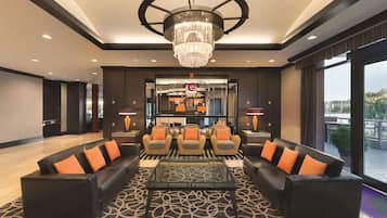 A lobby with a chandelier, leather sofas with orange cushions, a patterned carpet, and a reception desk.