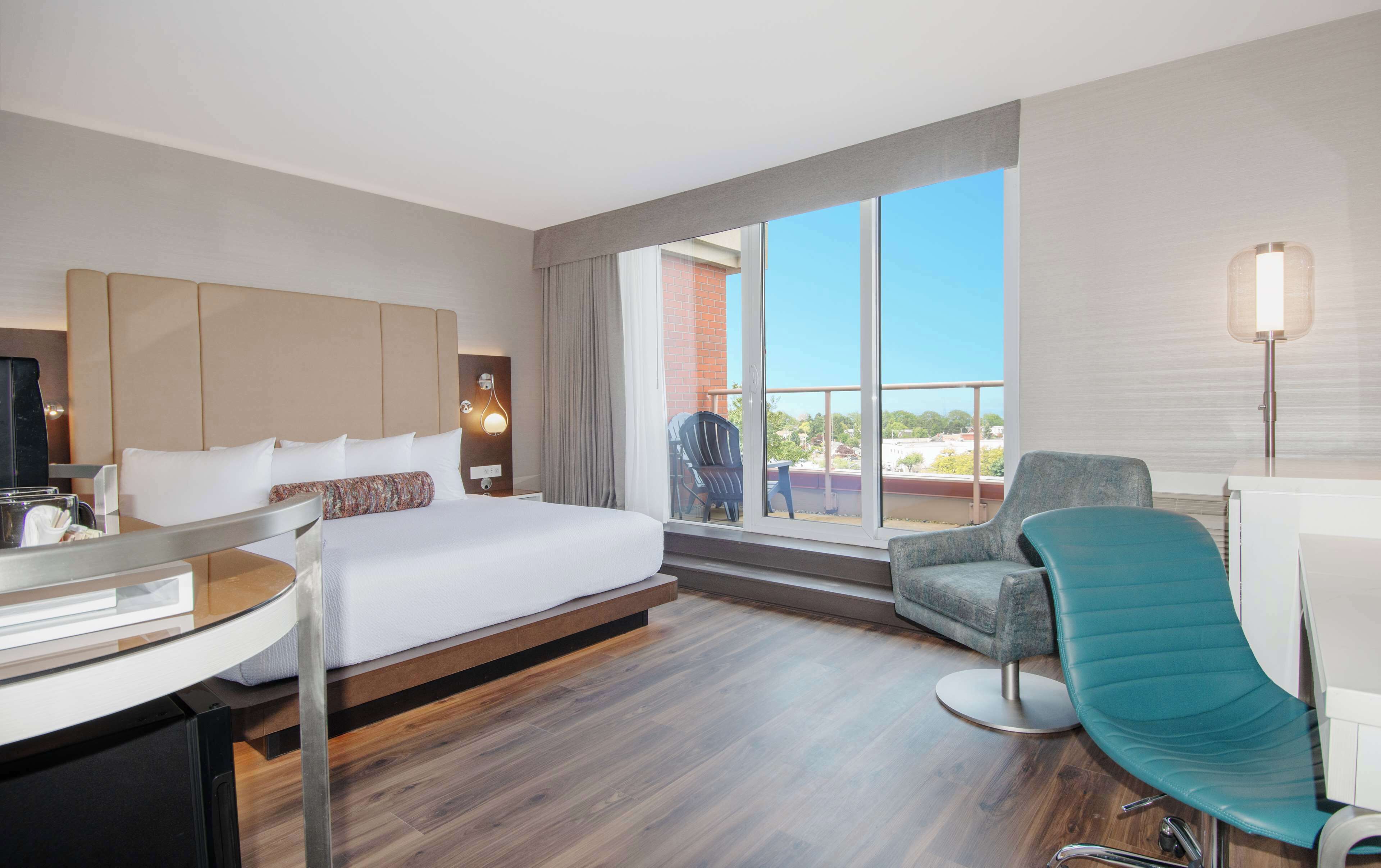 A hotel room with a large bed, a desk, a chair, and a balcony with a view.