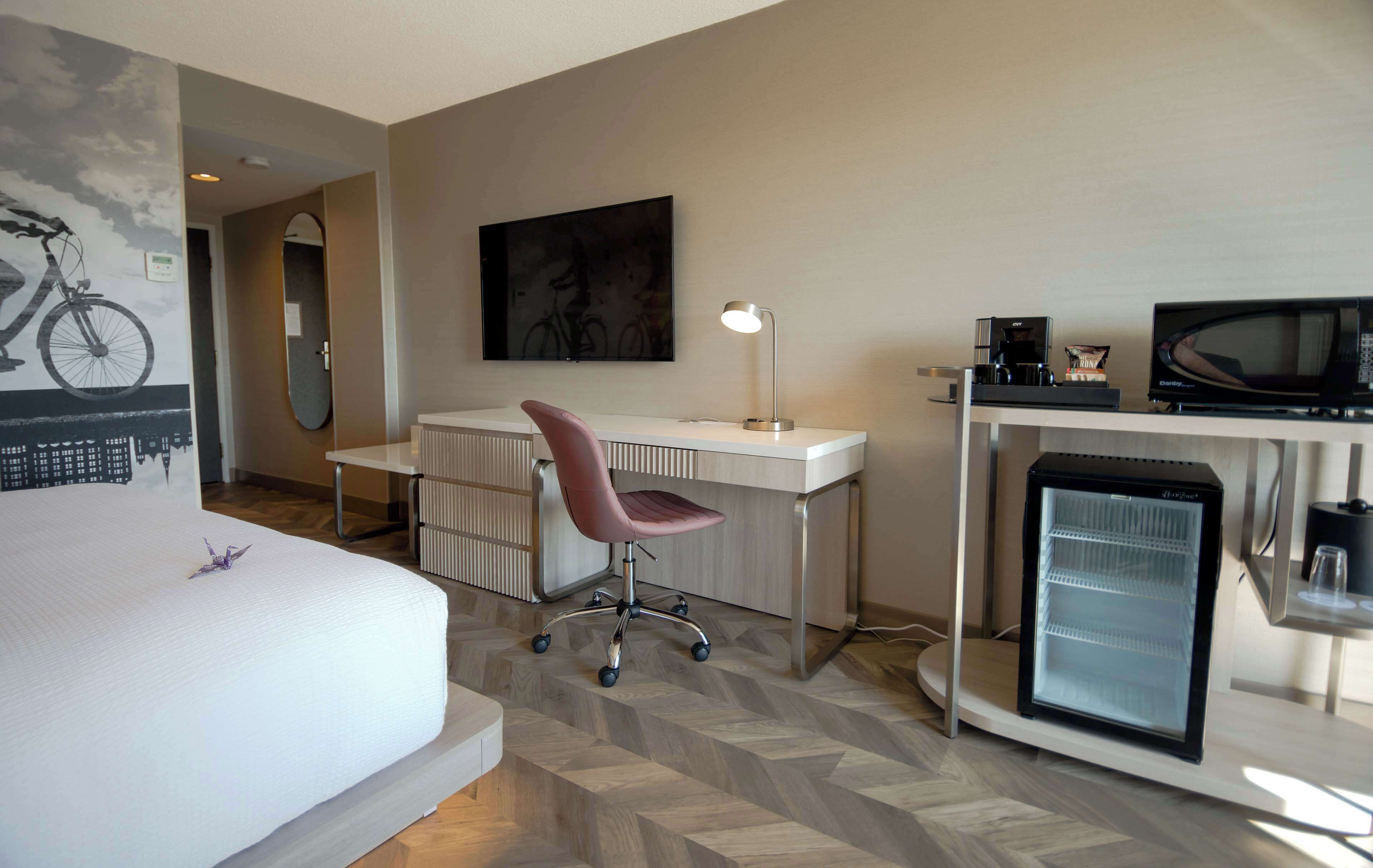 Une chambre d’hôtel comprenant un lit, un bureau avec une chaise, un réfrigérateur, un four à micro-ondes et un miroir fixé au mur.