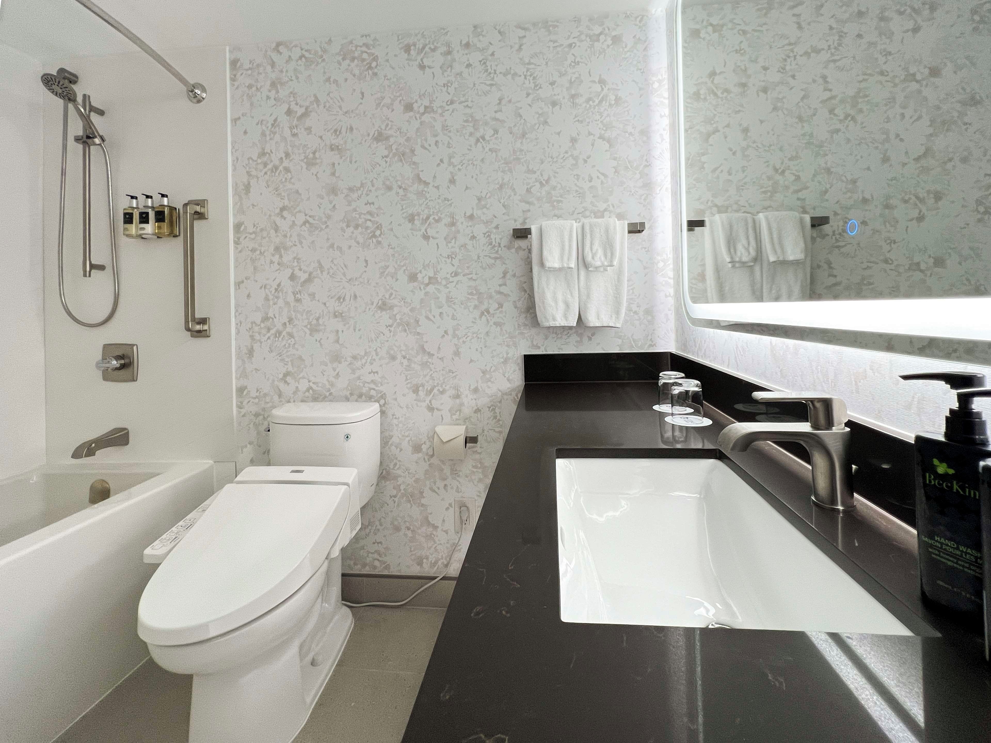 Ein modernes Badezimmer mit Toilette, Bidet, Dusche und einem großen Spiegel über dem Waschbecken.