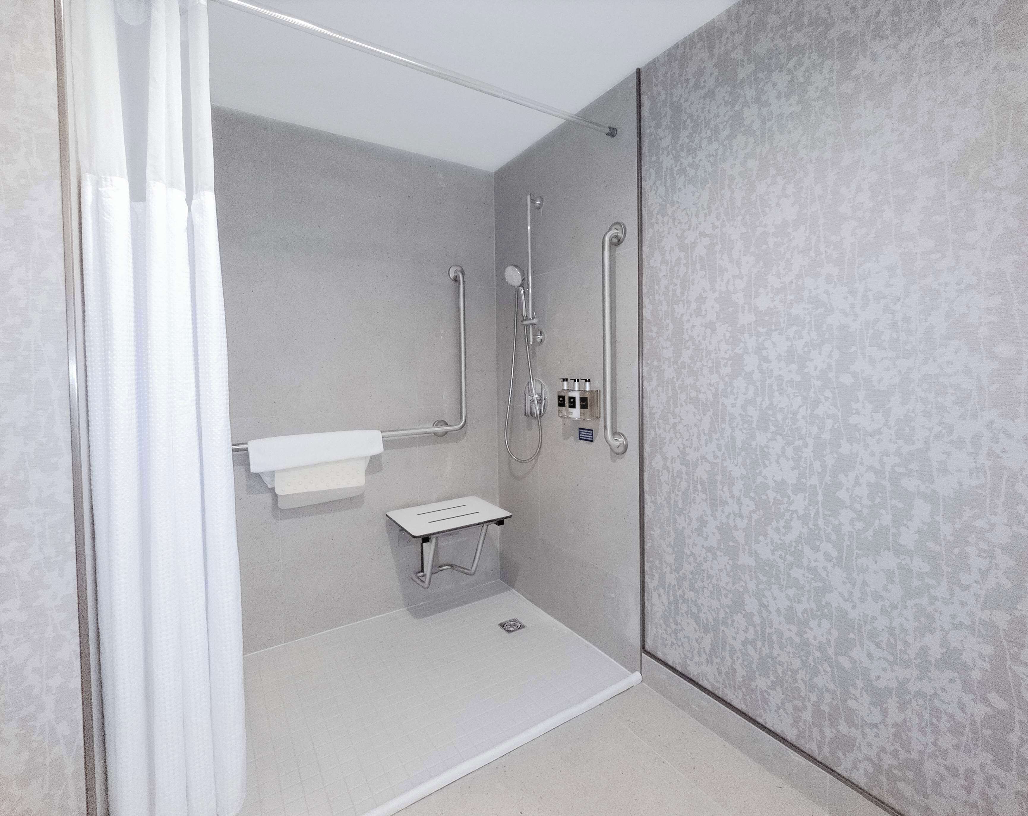 A shower room with a grab bar, a white sink, and a textured wall.