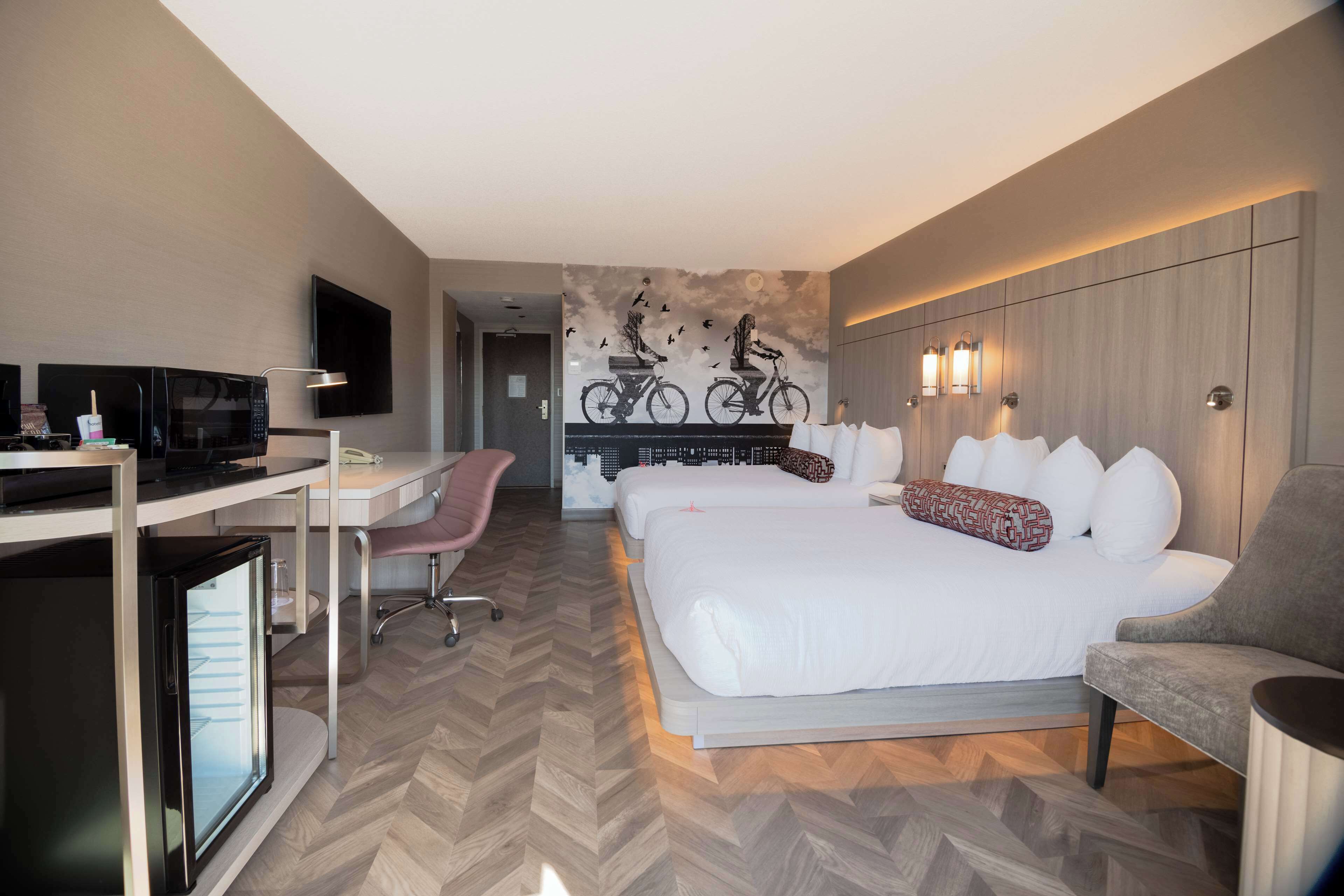 A hotel room with a bed, desk, chair, television, and a wall mural.