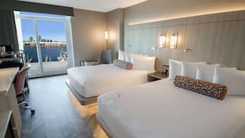 Habitación de hotel con dos camas, un escritorio, una silla y vista al puerto deportivo.
