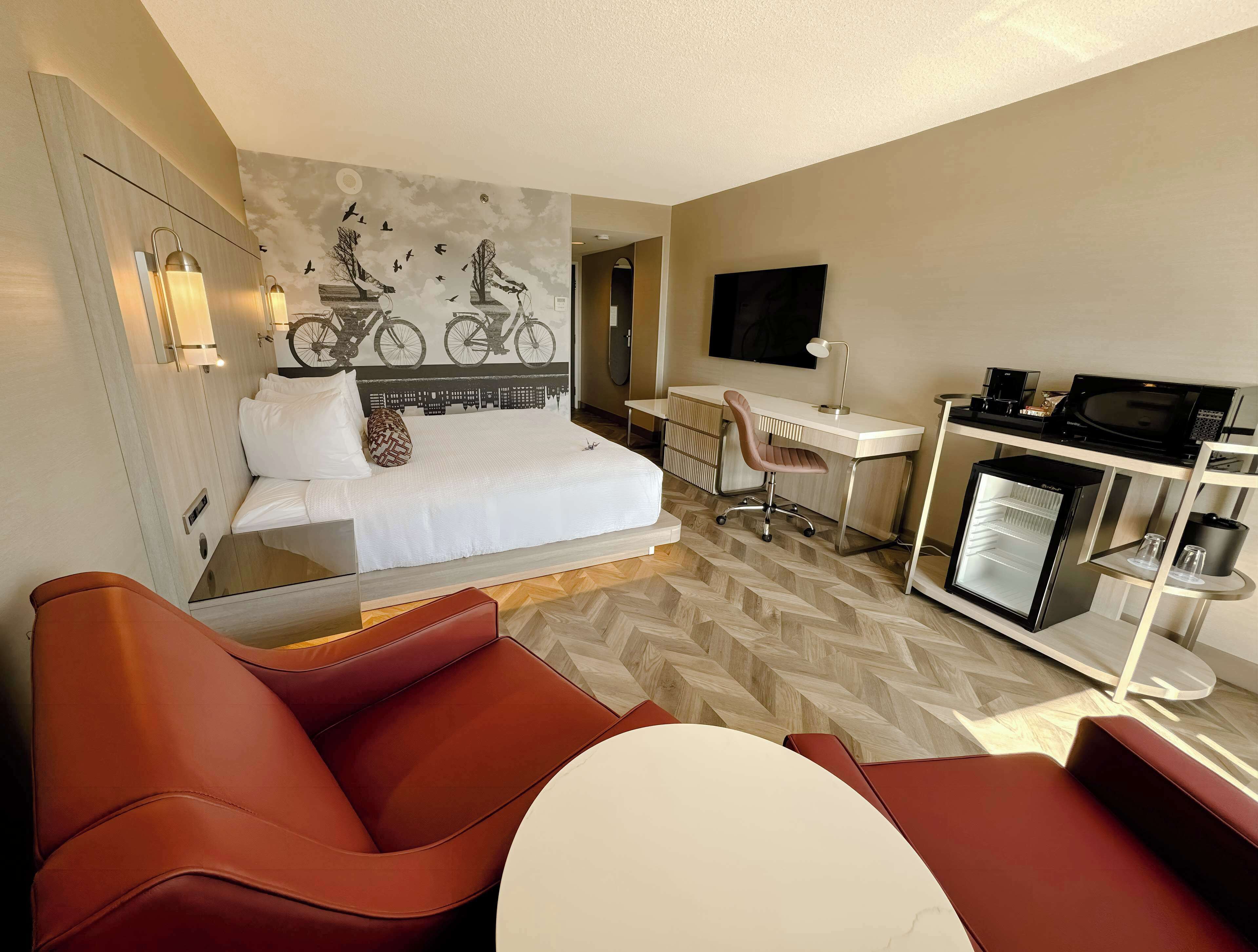 Habitación de hotel con cama, escritorio, silla, televisor y minibar.