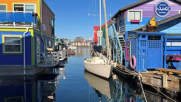 A narrow waterway with colorful buildings on either side, including a blue building with a sign for 'Artisans 4 Winds Nest Boutique' and a 'Pottery' sign.