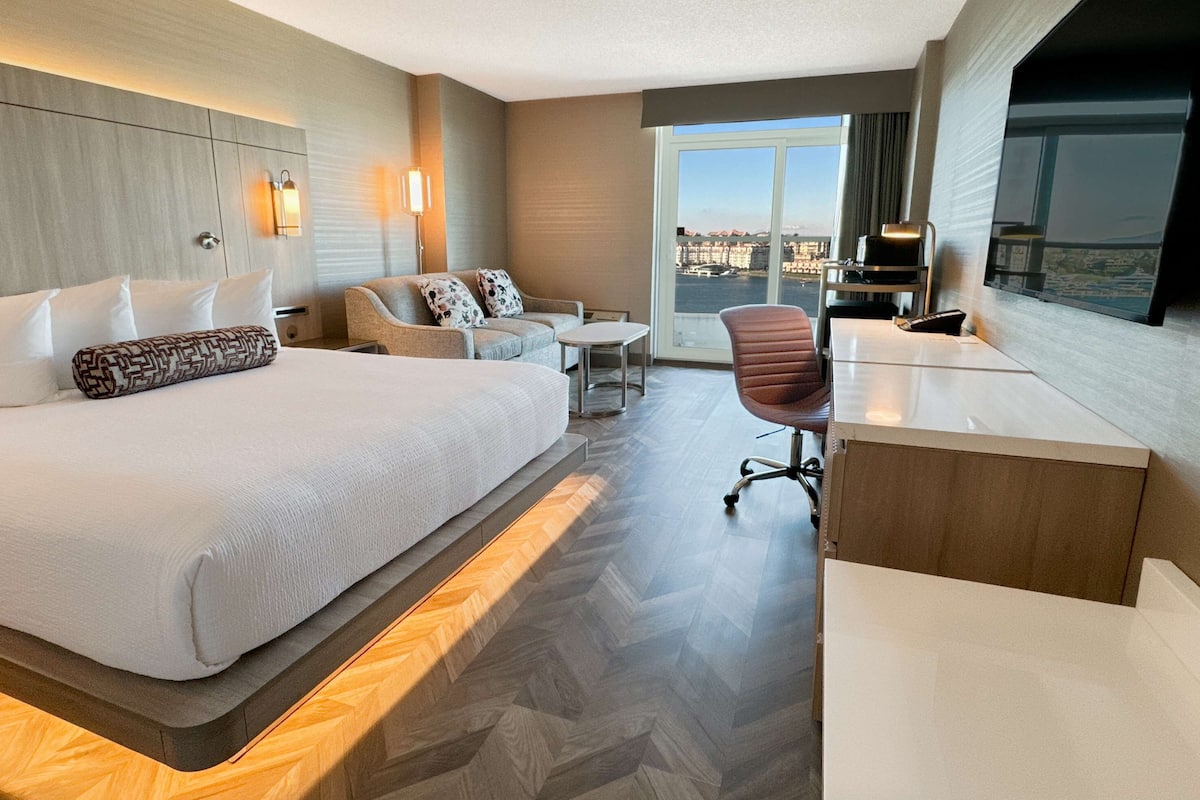 Habitación de hotel con una cama grande, un sofá, un escritorio y vistas a la ciudad.
