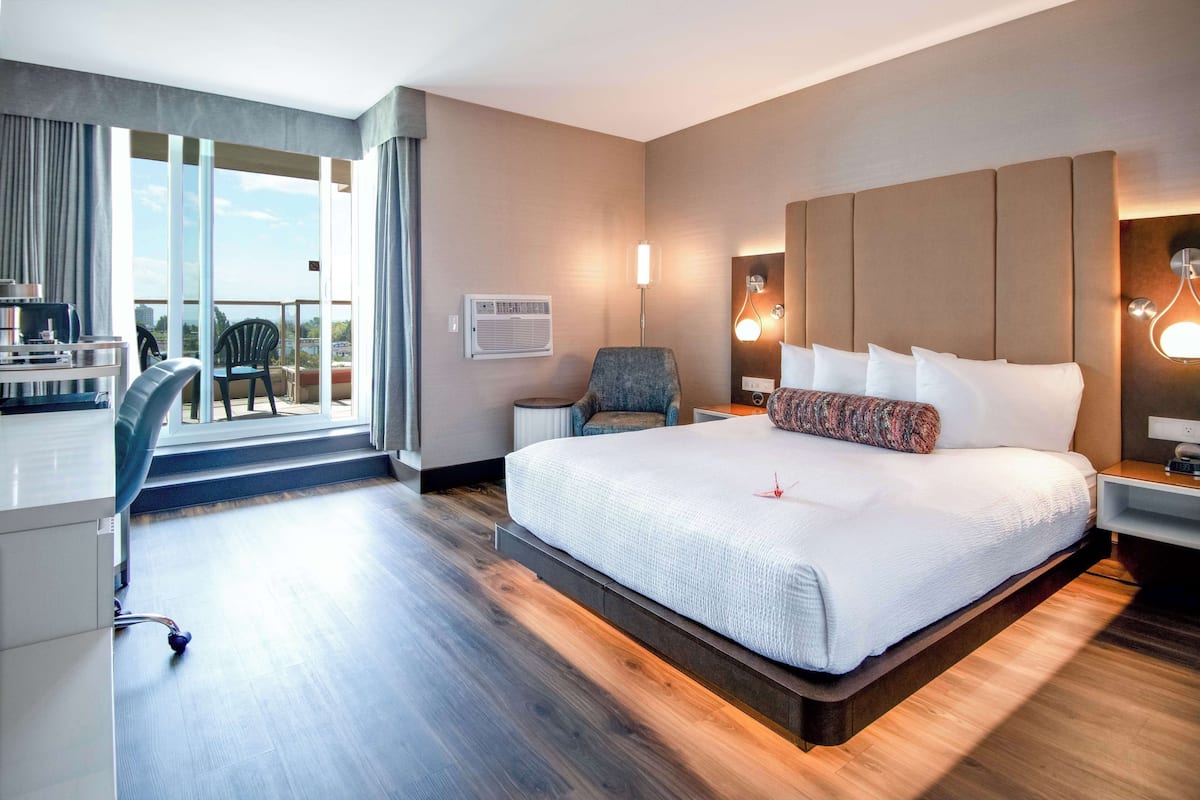 Moderni hotellihuone, jossa on suuri sänky, työpöytä ja tuoli. Huoneessa on myös parveke, jolta on näkymä.