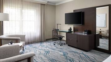 Une chambre d’hôtel dotée d’un grand téléviseur à écran plat fixé au mur, d’un bureau avec une chaise, d’un canapé et d’une moquette à motifs.