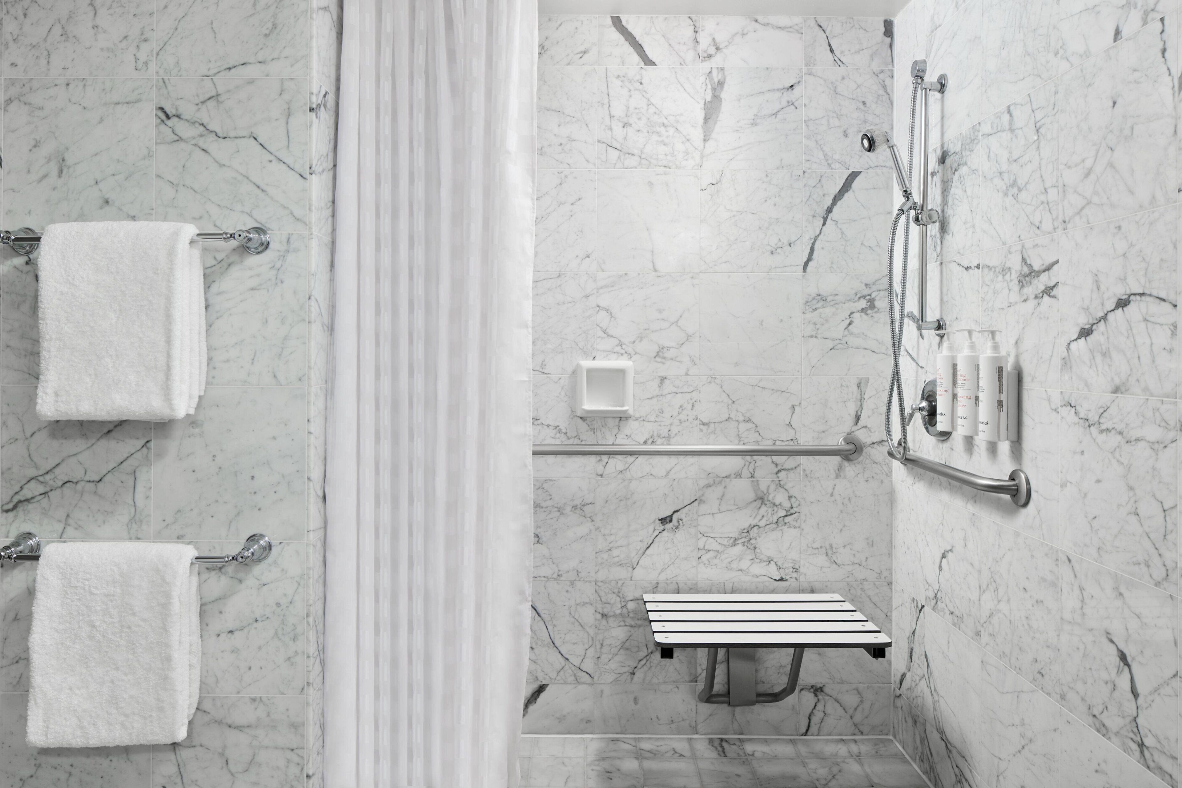A modern bathroom with marble walls, a shower with a handheld showerhead, and a bench.