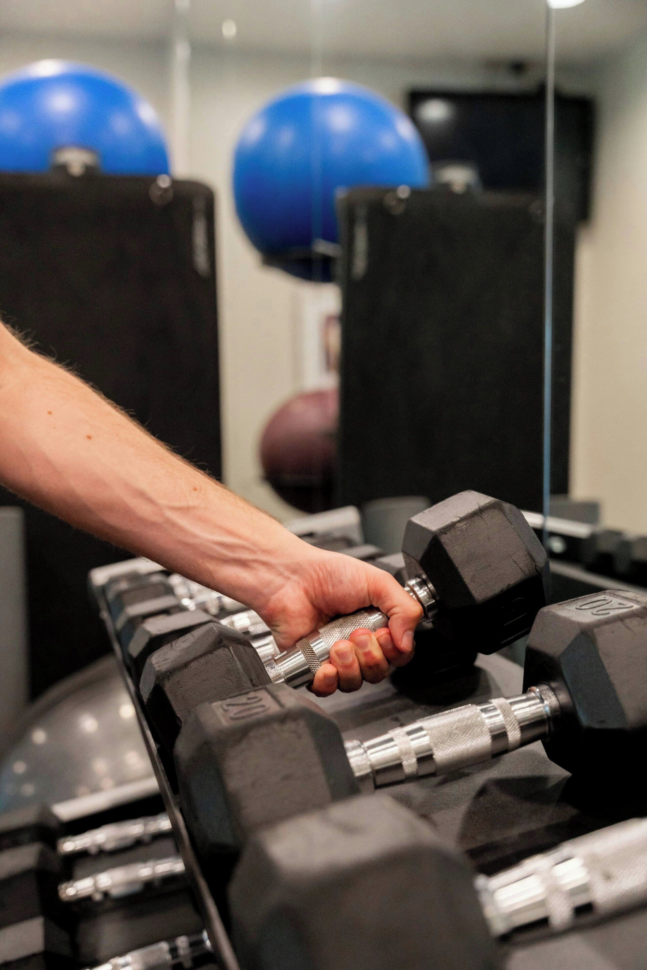 A hand gripping a dumbbell in a gym setting with exercise balls in the background.