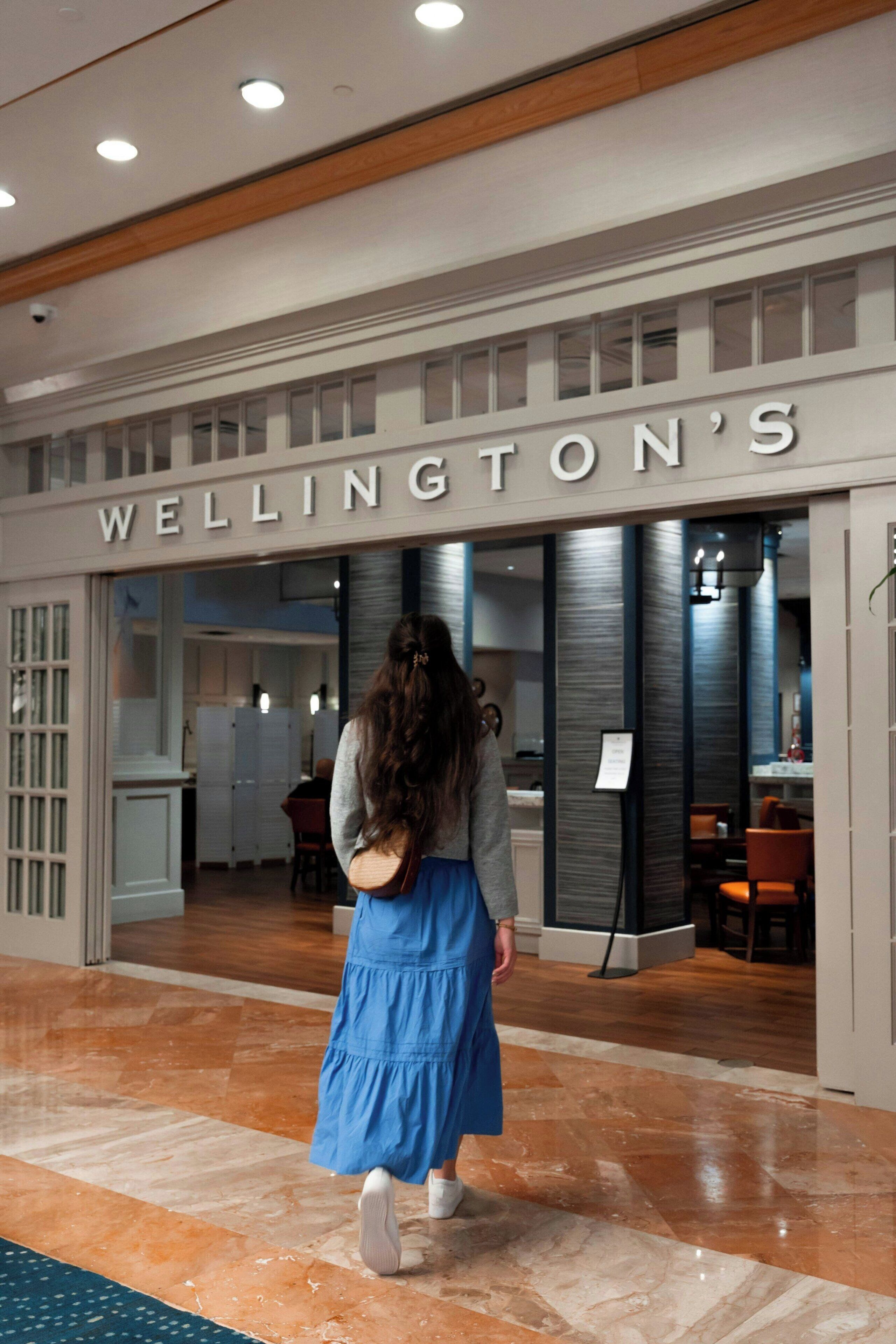Una donna cammina verso l'ingresso di un hotel con la scritta "Wellington's".