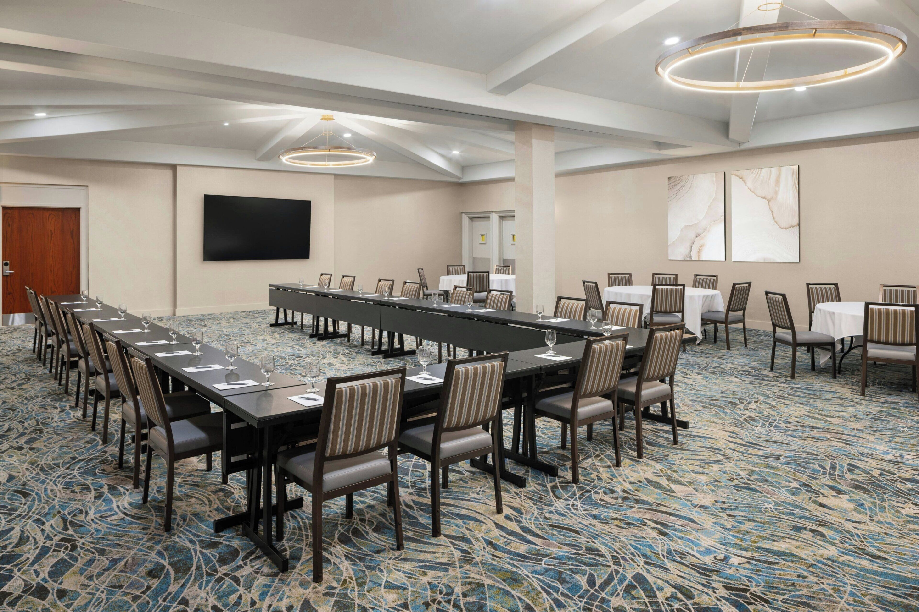 A conference room with a long table, chairs, a flat-screen TV, and a patterned carpet.