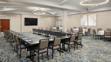 A conference room with a long table, chairs, a flat-screen TV, and a patterned carpet.