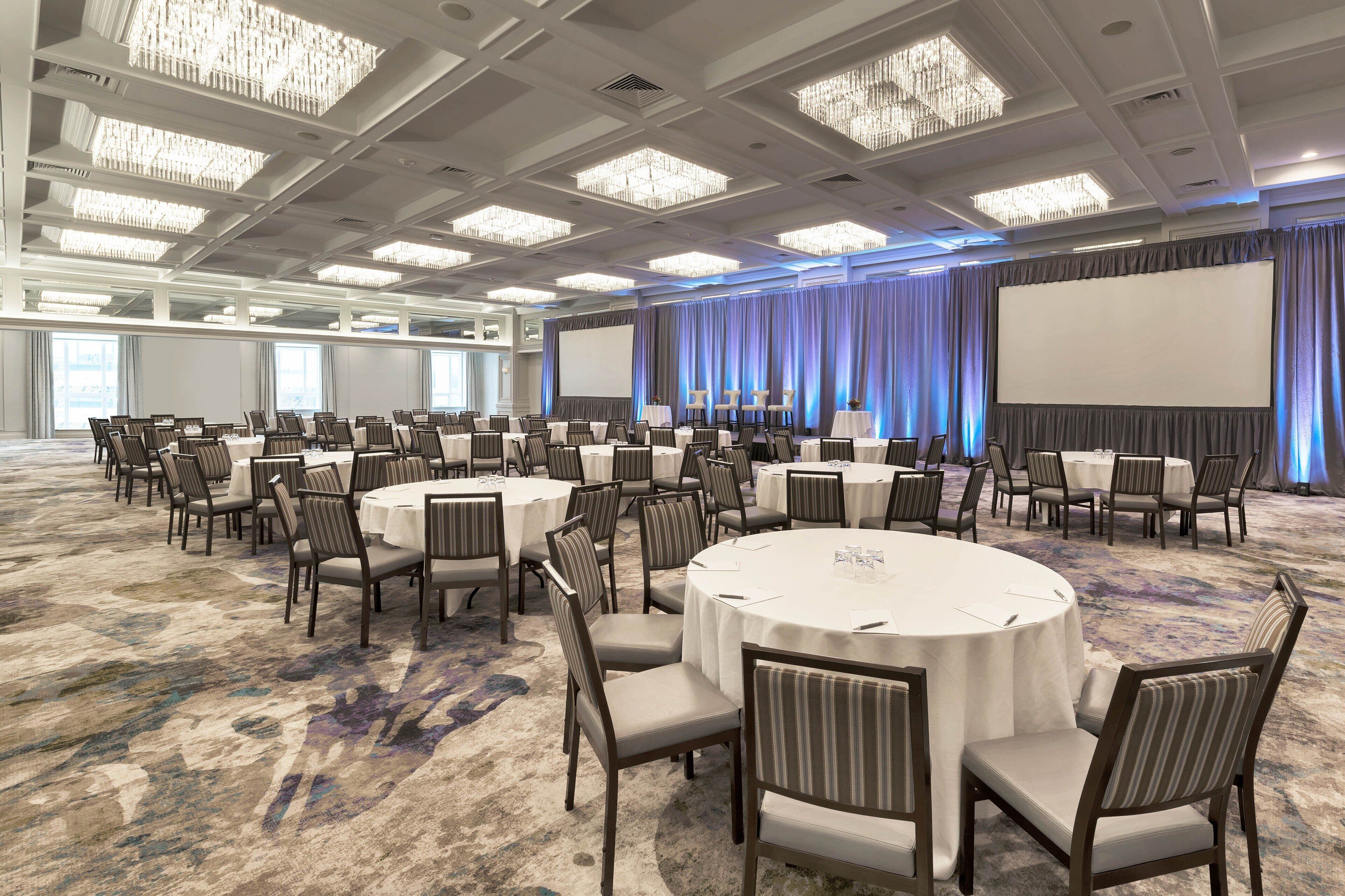 A large conference room with round tables and chairs, a large screen, and a chandelier.