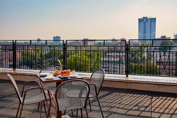 A terrace with a table set for two, chairs, and a view of the cityscape.