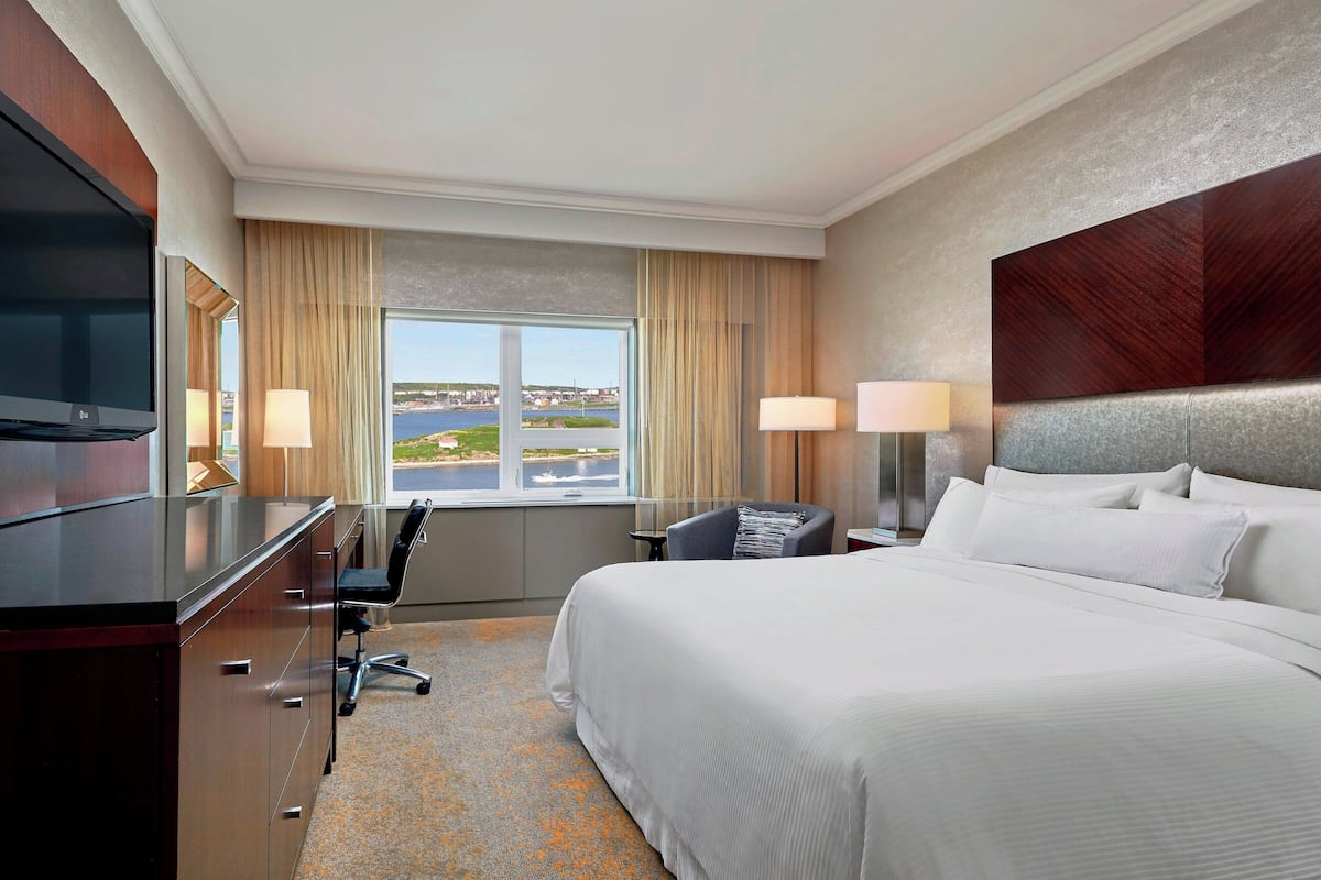 A hotel room with a bed, desk, chair, lamps, and a TV.