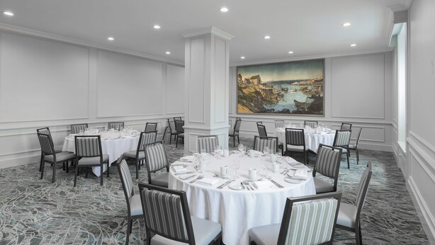 Un salón de conferencias con mesas redondas, sillas y un cuadro grande en la pared.