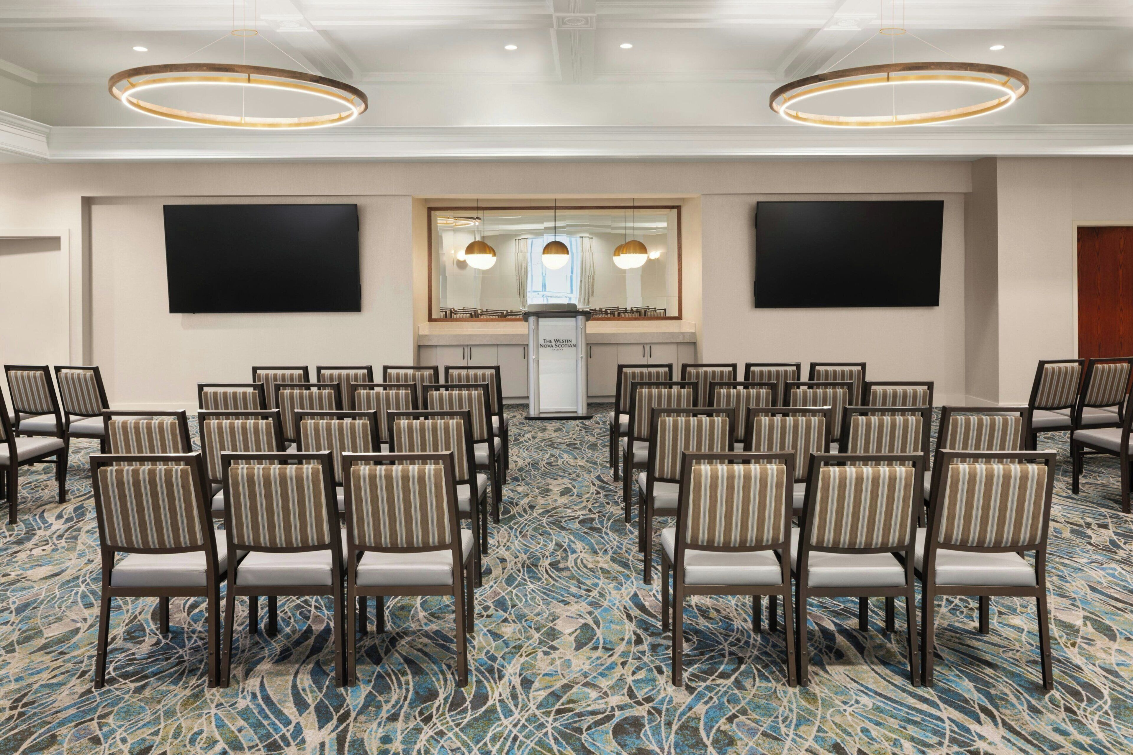 A conference room with rows of chairs, a podium, and two large screens.