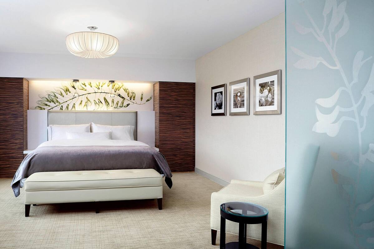 A modern bedroom with a large bed, a bench, a small table, and a chandelier.