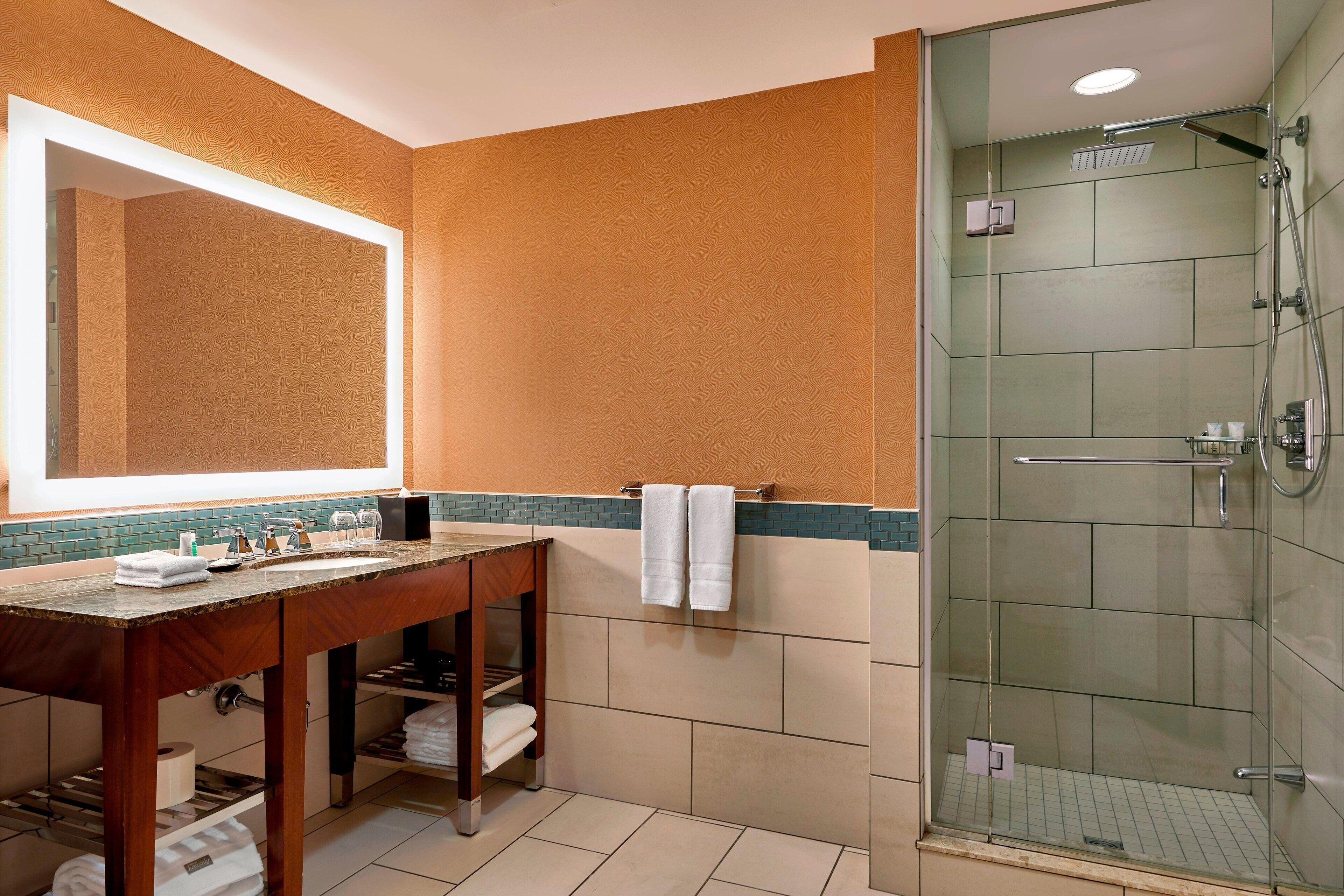A bathroom with a wooden vanity, a large mirror, a glass-enclosed shower, and a tiled floor.