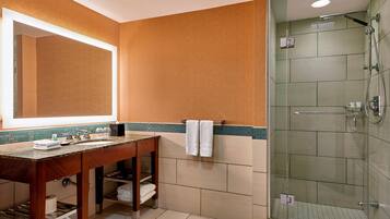 A bathroom with a wooden vanity, a large mirror, a glass-enclosed shower, and a tiled floor.
