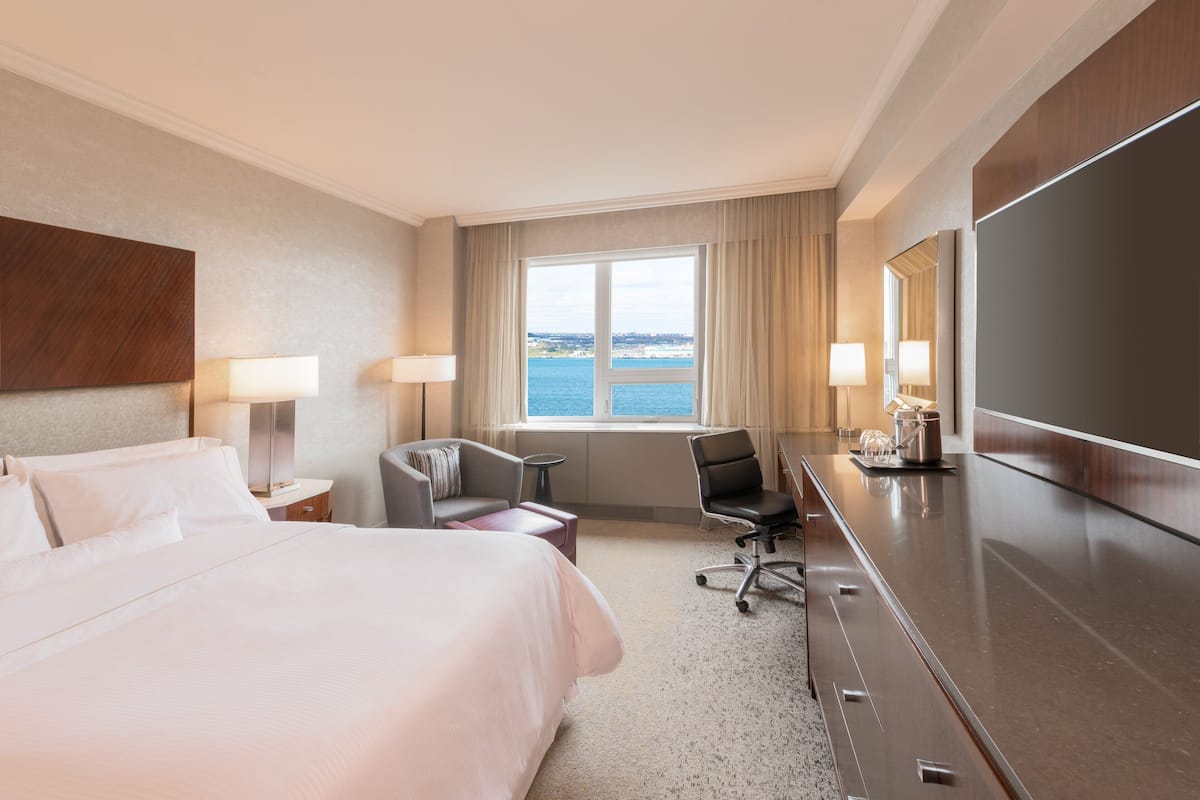A hotel room with a bed, a desk, a chair, a TV, and a view of the sea.