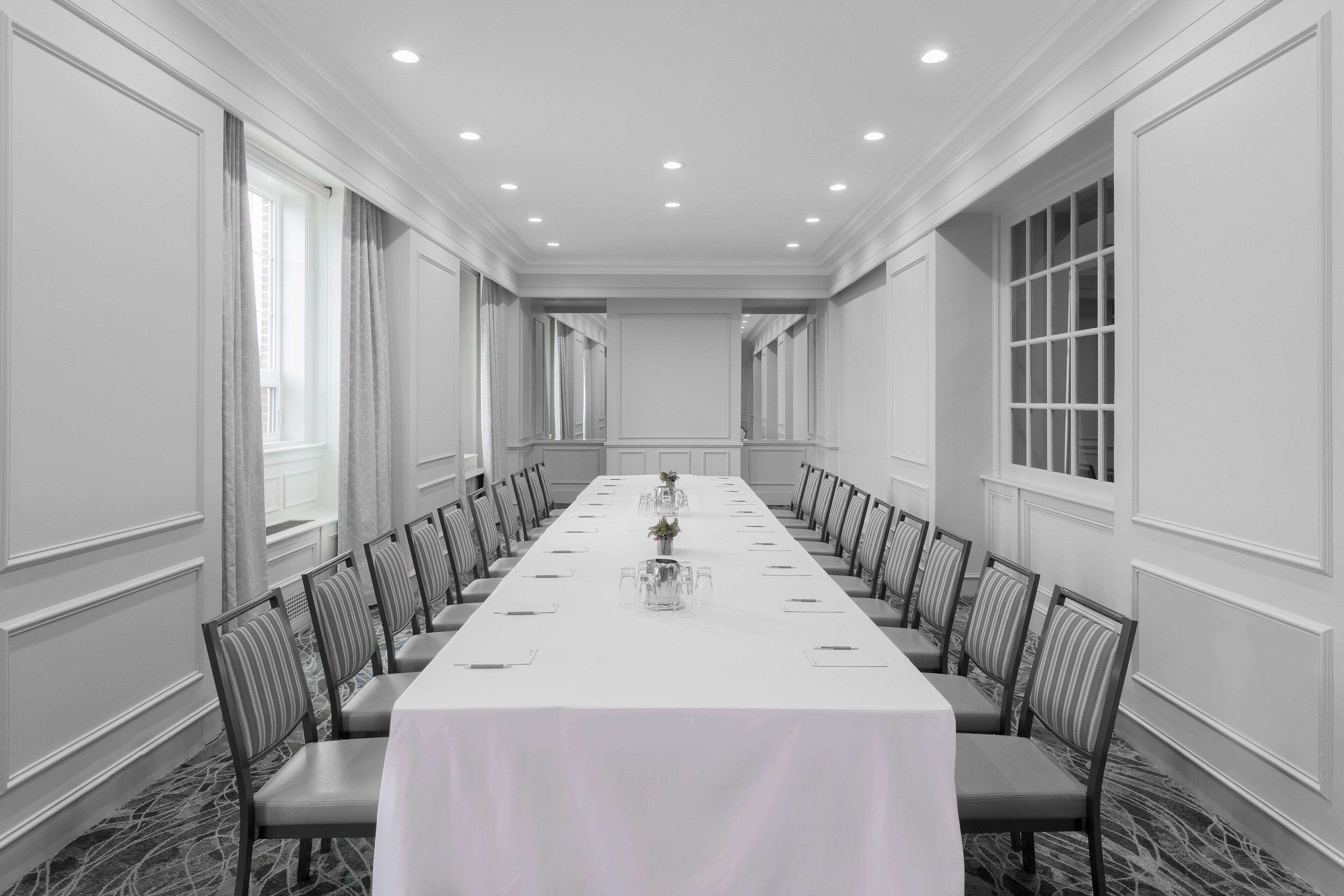 Une salle de conférence avec une longue table, des chaises et une nappe blanche.