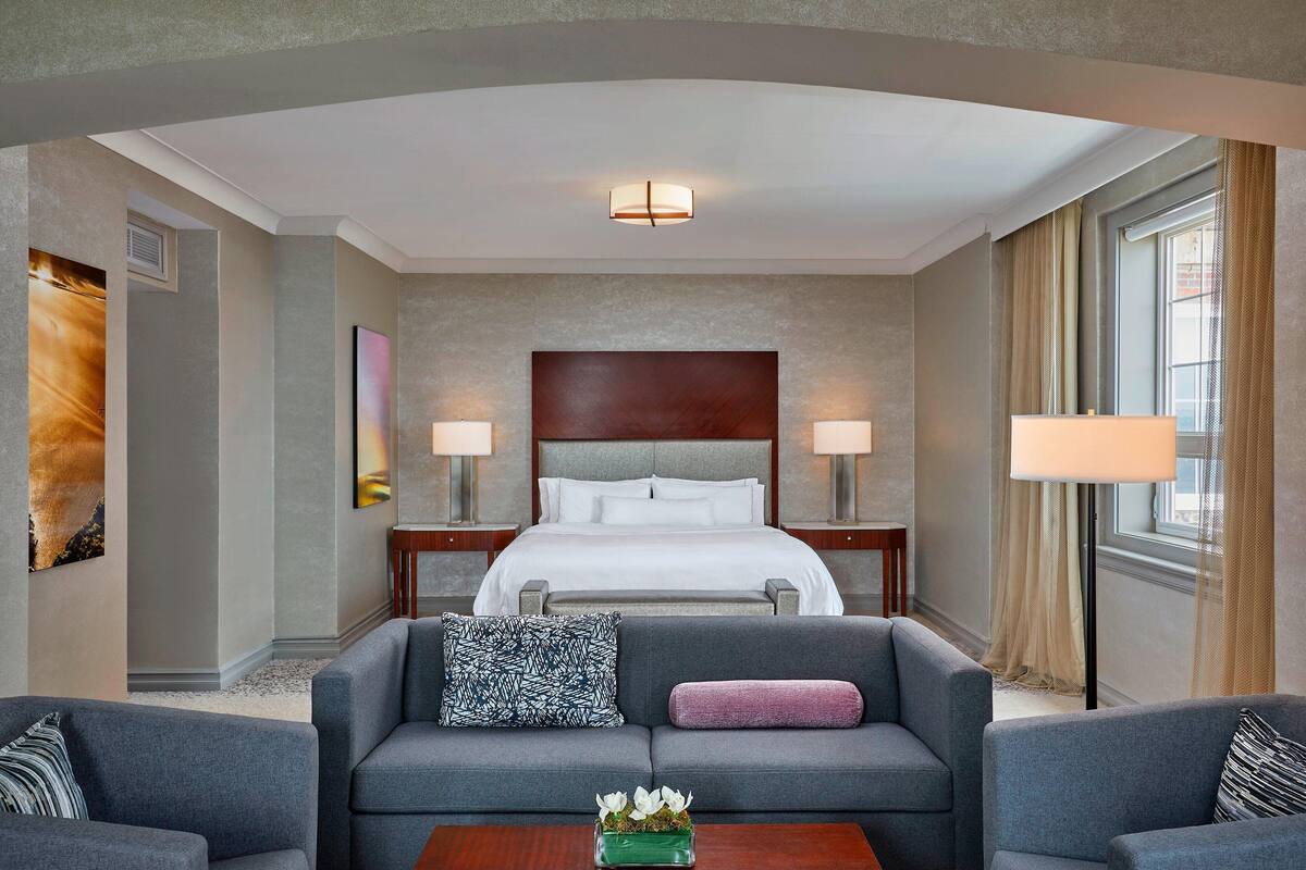 A hotel room with a large bed, two bedside lamps, a sofa, and a coffee table.