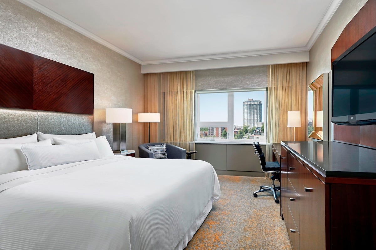 A hotel room with a large bed, a desk with a chair, a flat-screen TV, and a window with curtains.