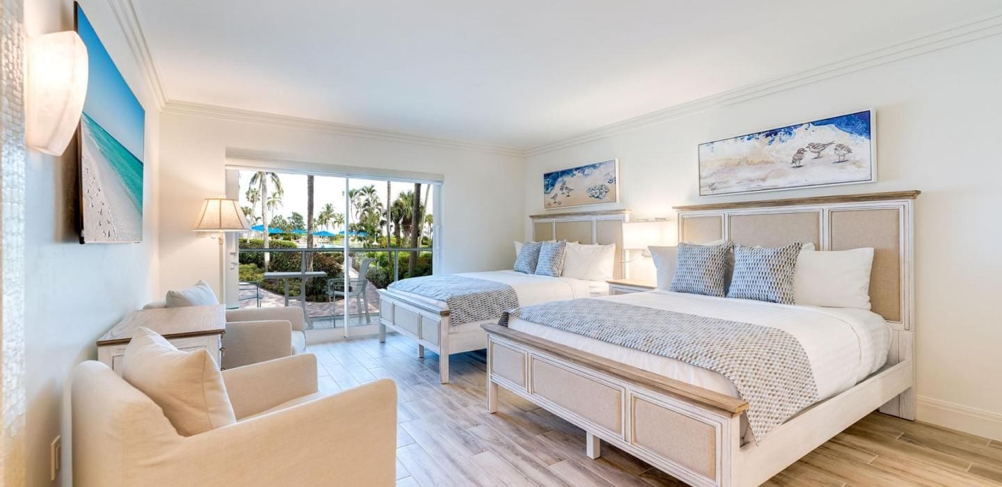 Habitación de hotel con una cama grande, un escritorio, una silla y un balcón con vistas a palmeras.
