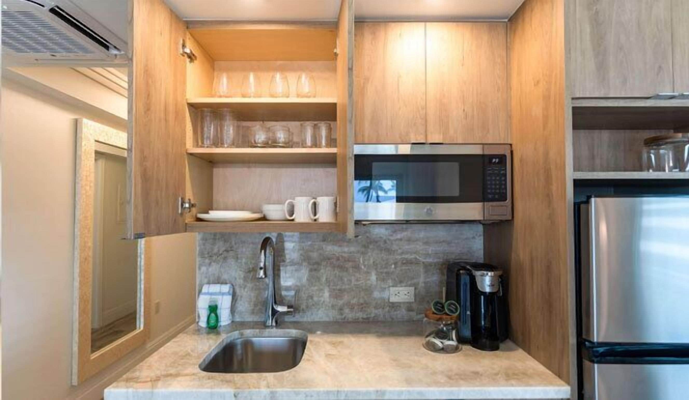 A compact kitchen with a stainless steel refrigerator, a microwave, a coffee maker, and a sink.
