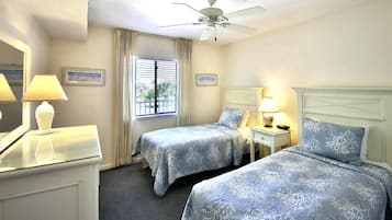 Ein Hotelzimmer mit zwei Betten, einem Deckenventilator, einem Fenster mit Vorhängen, einem Schminktisch und Nachttischlampen.