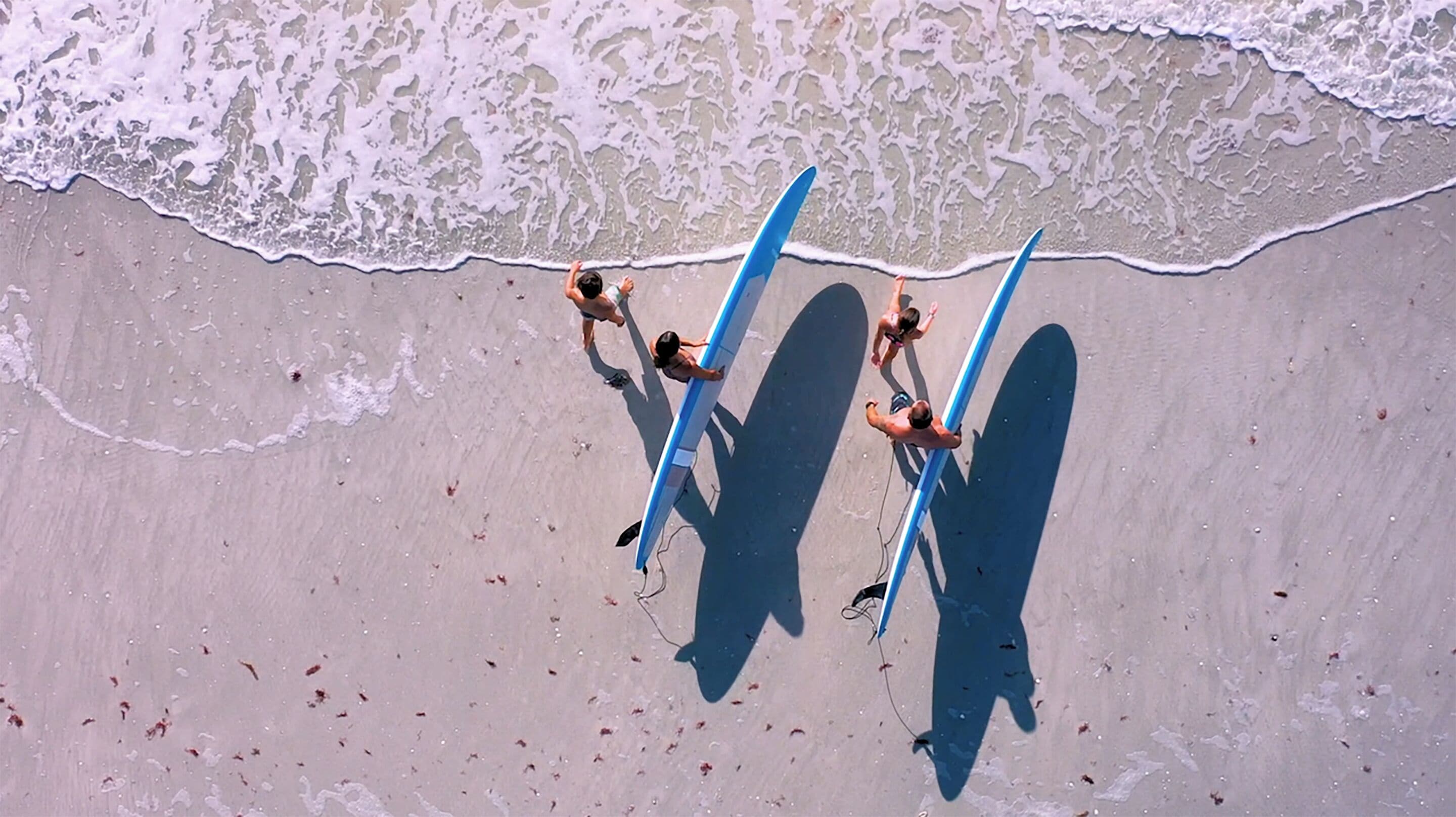 An aerial view of a beach with people holding surfboards.