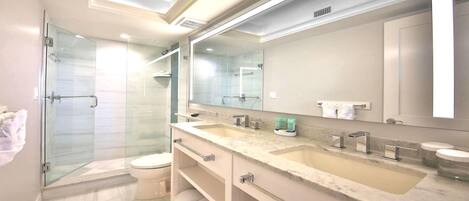 Un bany modern amb una dutxa envidriada, un vàter, un lavabo doble i un mirall gran.