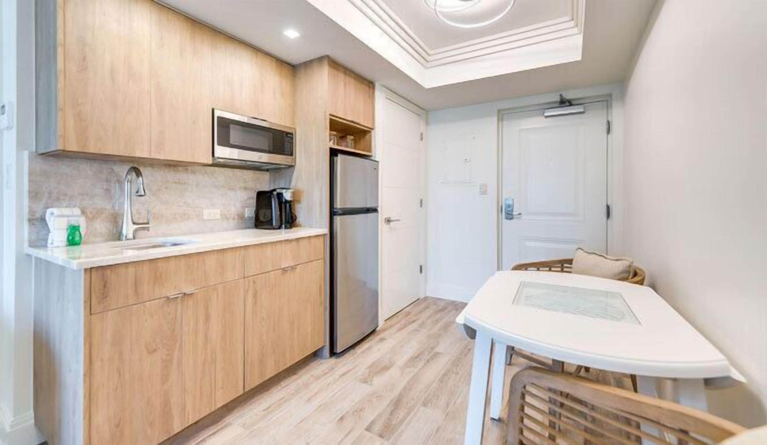 A compact kitchen with wooden cabinets, a microwave, a refrigerator, and a small dining table.