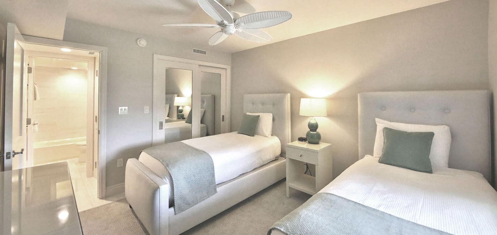 Une chambre d’hôtel avec deux lits, un ventilateur de plafond, une table de chevet avec une lampe et un miroir.