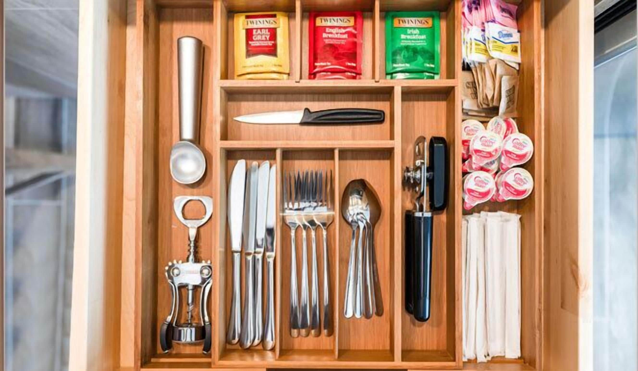 A kitchen drawer with various utensils, including a knife, spoons, forks, and a bottle opener.